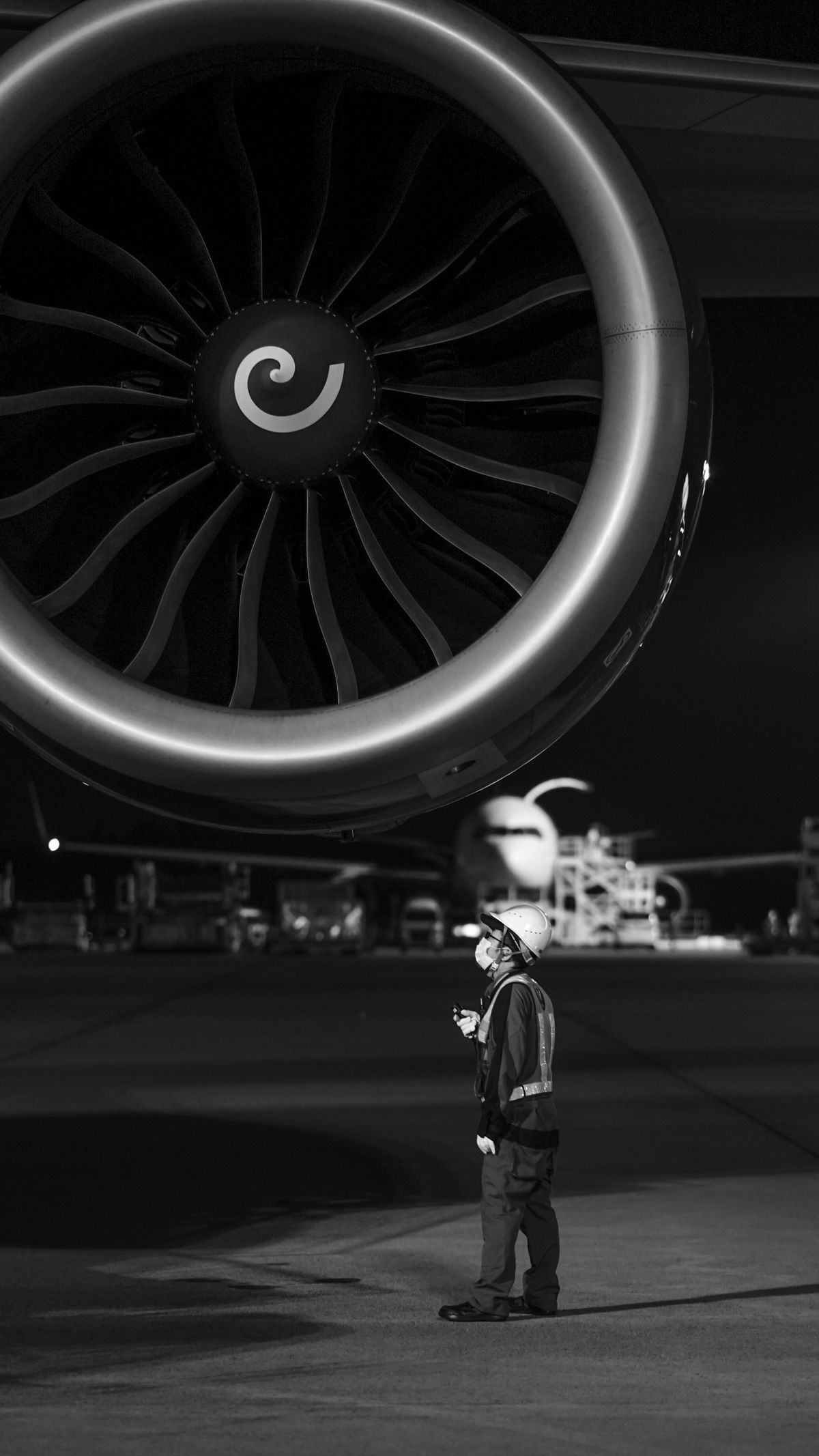 A technician in a hard hat looking up at a jet engine on the apron at night
