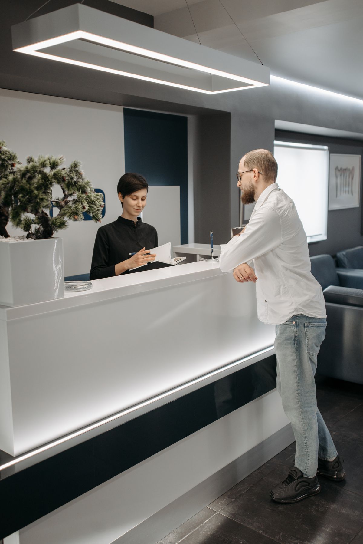 A receptionist taking a note for a visitor at an office front desk